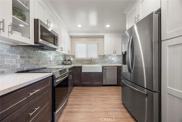 kitchen featuring white cabinets, glass insert cabinets, a sink, appliances with stainless steel finishes, and dark brown cabinets