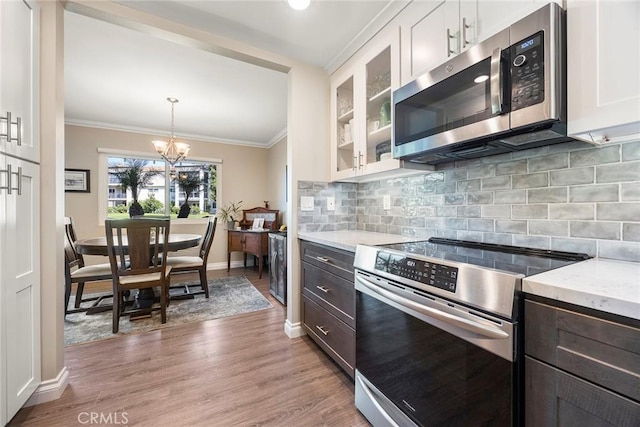 kitchen featuring glass insert cabinets, white cabinetry, baseboards, ornamental molding, and appliances with stainless steel finishes