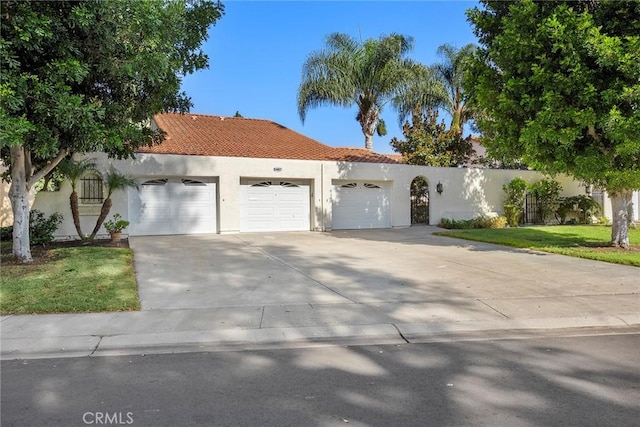 mediterranean / spanish-style house featuring concrete driveway, a tile roof, a front yard, an attached garage, and stucco siding