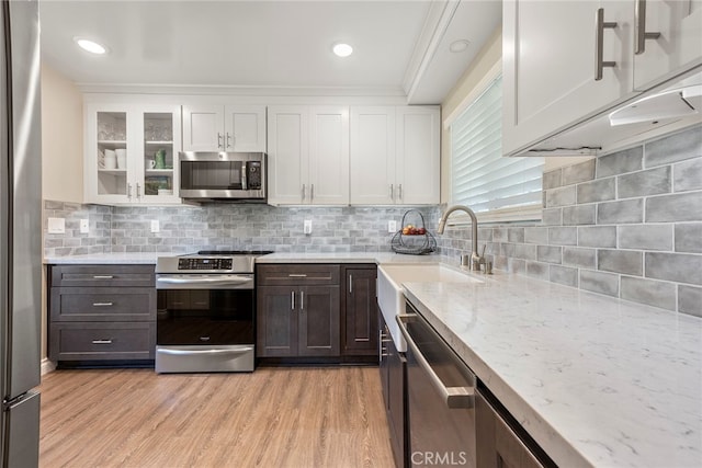 kitchen featuring white cabinets, ornamental molding, stainless steel appliances, light wood-type flooring, and decorative backsplash