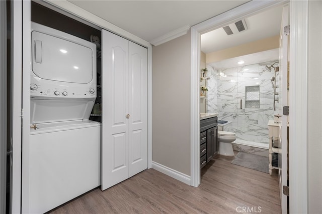 clothes washing area with stacked washer and dryer, ornamental molding, and light hardwood / wood-style floors