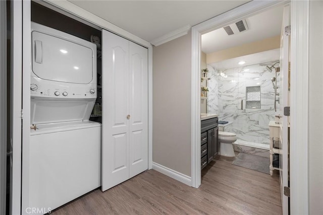 washroom featuring stacked washer / drying machine, laundry area, visible vents, baseboards, and wood finished floors