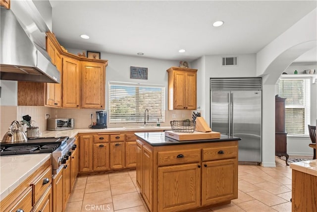 kitchen with sink, wall chimney range hood, decorative backsplash, a kitchen island, and appliances with stainless steel finishes