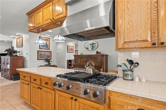 kitchen with wall chimney range hood, stainless steel gas cooktop, tasteful backsplash, tile countertops, and light tile patterned flooring