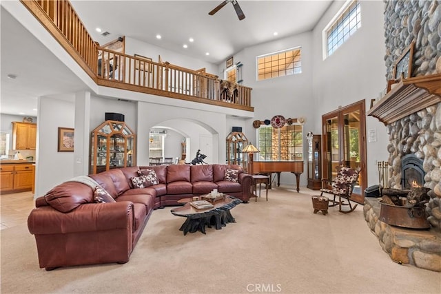 living room with ceiling fan, light colored carpet, a towering ceiling, and a fireplace