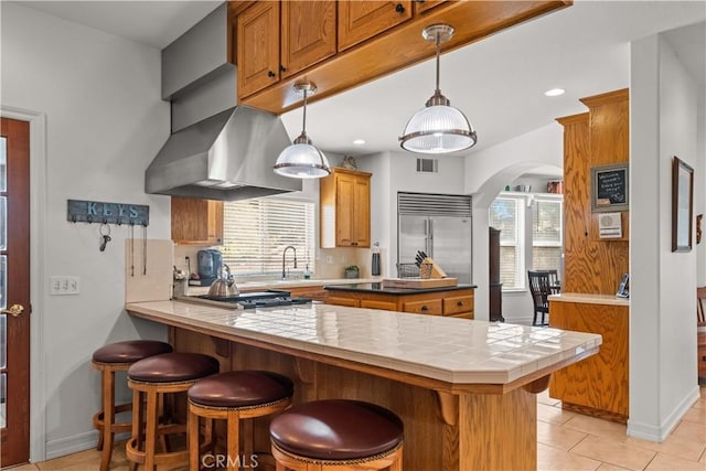 kitchen featuring kitchen peninsula, appliances with stainless steel finishes, light tile patterned floors, decorative light fixtures, and tile counters