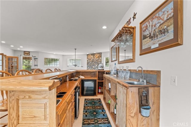 kitchen featuring sink, beverage cooler, wood counters, kitchen peninsula, and a kitchen bar