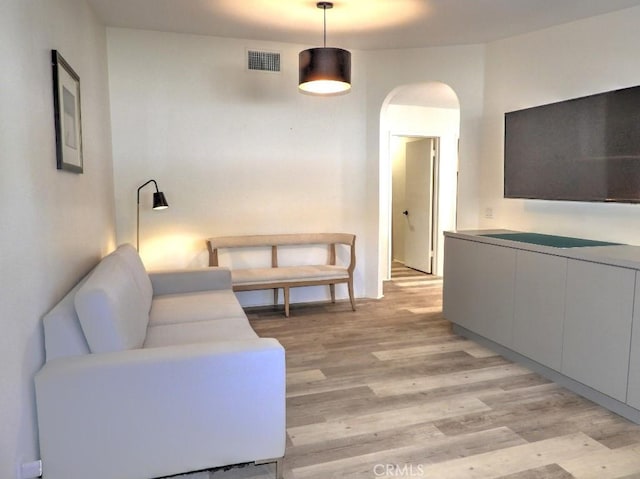 living room featuring arched walkways, light wood-type flooring, and visible vents