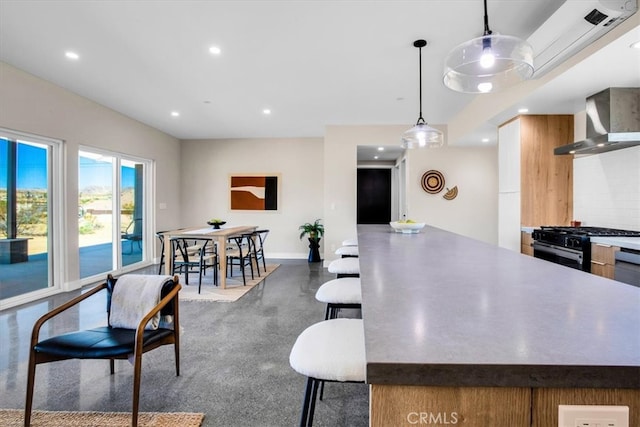 kitchen featuring pendant lighting, tasteful backsplash, wall chimney range hood, a breakfast bar area, and black range with gas stovetop