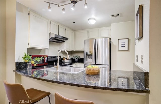 kitchen featuring kitchen peninsula, appliances with stainless steel finishes, white cabinetry, dark stone counters, and sink