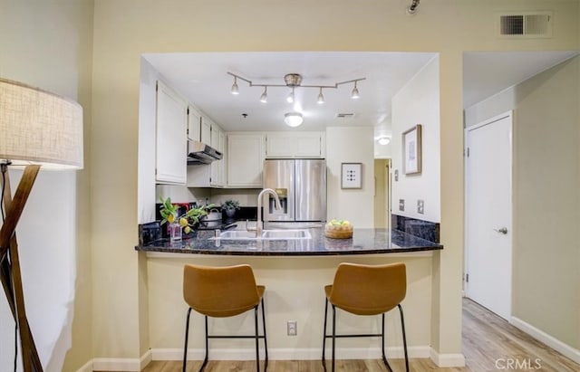 kitchen with kitchen peninsula, stainless steel fridge, white cabinetry, dark stone counters, and light hardwood / wood-style flooring