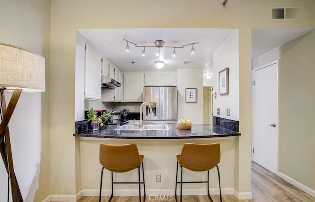kitchen featuring white cabinetry, visible vents, under cabinet range hood, a peninsula, and stainless steel fridge