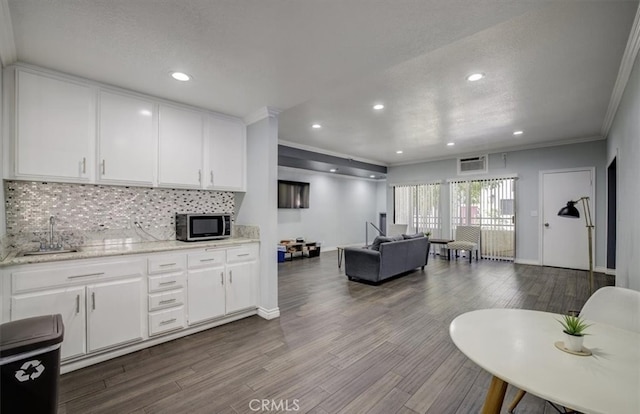kitchen featuring stainless steel microwave, decorative backsplash, white cabinets, a sink, and ornamental molding
