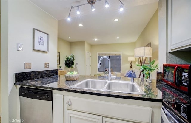 kitchen featuring dark stone counters, stainless steel appliances, a sink, white cabinetry, and a peninsula