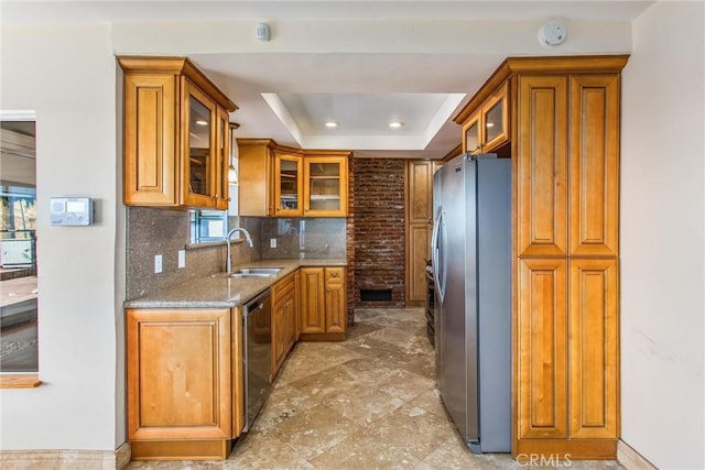 kitchen with sink, decorative backsplash, a tray ceiling, light stone counters, and stainless steel appliances