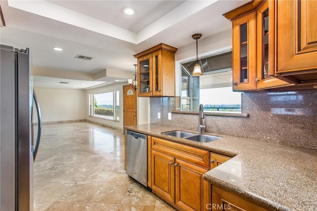 kitchen featuring backsplash, sink, appliances with stainless steel finishes, decorative light fixtures, and light stone counters