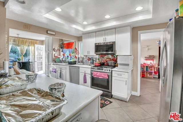 kitchen featuring white cabinetry, ornamental molding, stainless steel appliances, and a tray ceiling