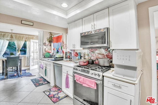 kitchen featuring light tile patterned flooring, a raised ceiling, white cabinetry, ornamental molding, and stainless steel appliances