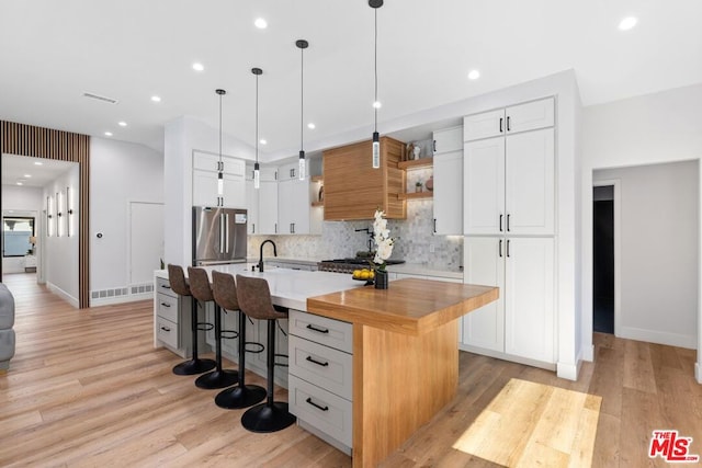 kitchen featuring light wood-type flooring, stainless steel refrigerator, white cabinetry, a center island with sink, and a kitchen breakfast bar