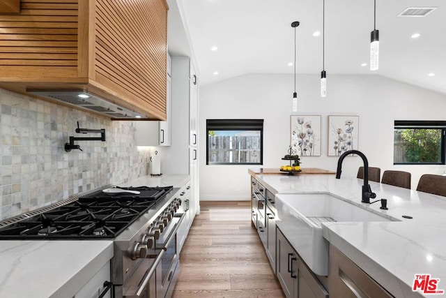 kitchen with light wood-type flooring, stainless steel range, decorative backsplash, hanging light fixtures, and lofted ceiling