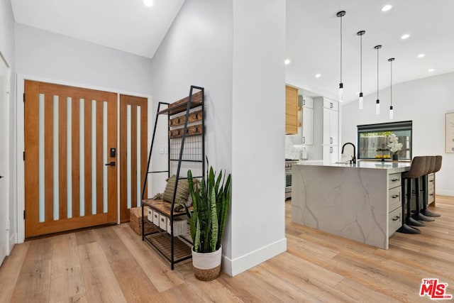 kitchen featuring light hardwood / wood-style floors, hanging light fixtures, vaulted ceiling, white cabinetry, and high end stove