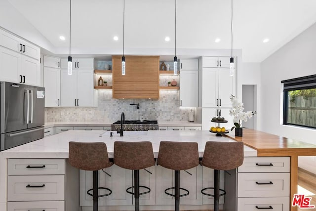 kitchen featuring light stone counters, white cabinets, hanging light fixtures, a center island with sink, and vaulted ceiling