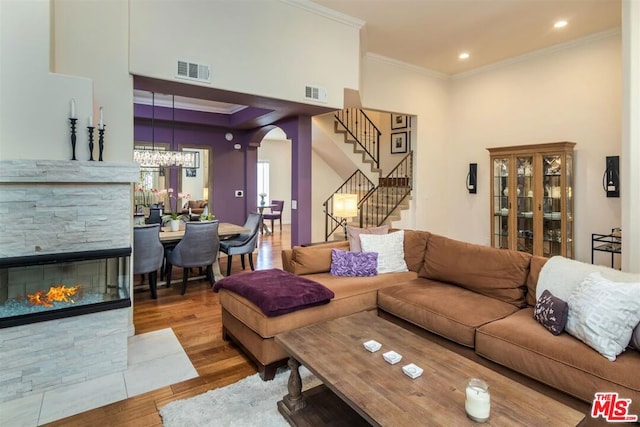 living room with crown molding, wood-type flooring, a stone fireplace, and a chandelier