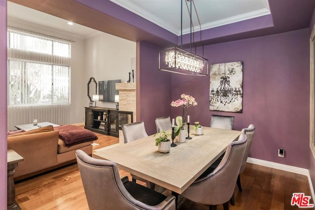 dining area with a raised ceiling, wood-type flooring, and crown molding