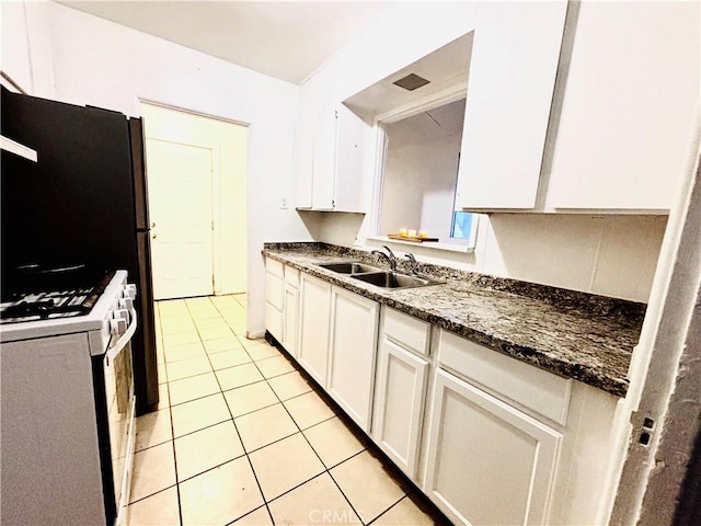 kitchen featuring white cabinetry, white gas stove, sink, dark stone countertops, and light tile patterned floors