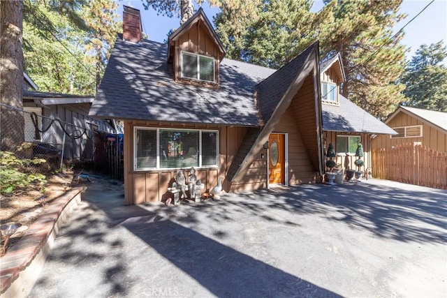 view of front of property featuring a shingled roof, board and batten siding, a chimney, and fence