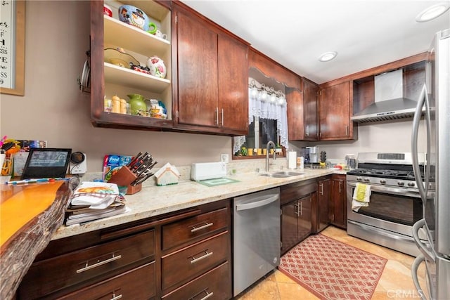 kitchen with light tile patterned floors, appliances with stainless steel finishes, a sink, wall chimney range hood, and light stone countertops