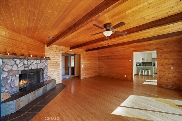 unfurnished living room with wood ceiling, wooden walls, a stone fireplace, wood finished floors, and beamed ceiling