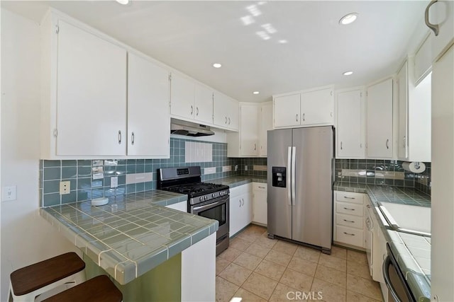 kitchen featuring stainless steel appliances, tile countertops, a peninsula, tasteful backsplash, and under cabinet range hood