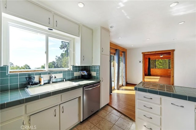 kitchen with a sink, decorative backsplash, stainless steel dishwasher, and tile countertops