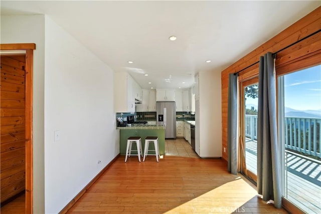 kitchen with a kitchen breakfast bar, a peninsula, stainless steel appliances, light wood-style floors, and white cabinetry