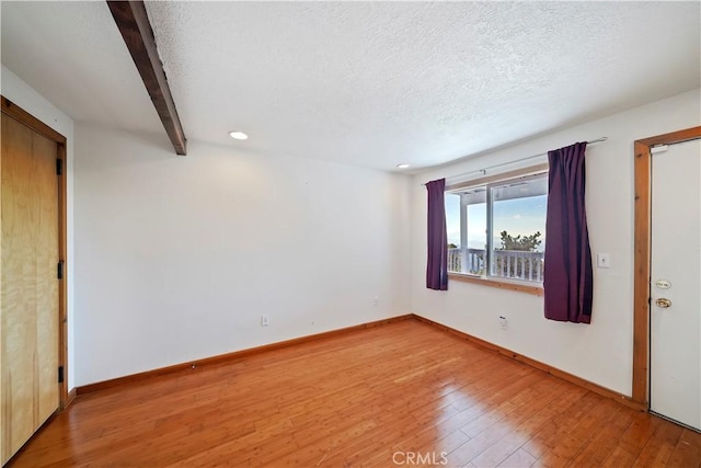 empty room featuring light wood-style floors, baseboards, and a textured ceiling