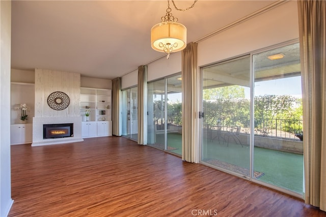 unfurnished living room featuring a brick fireplace, a wealth of natural light, built in features, and dark hardwood / wood-style floors