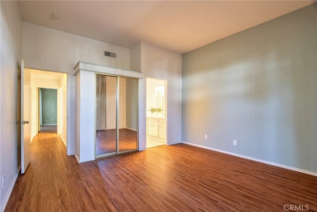 unfurnished bedroom featuring ensuite bathroom, a closet, and hardwood / wood-style floors