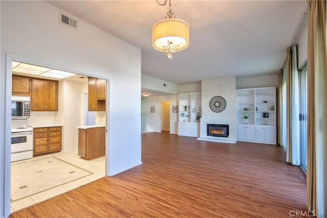 kitchen featuring light hardwood / wood-style floors, electric stove, hanging light fixtures, and a fireplace