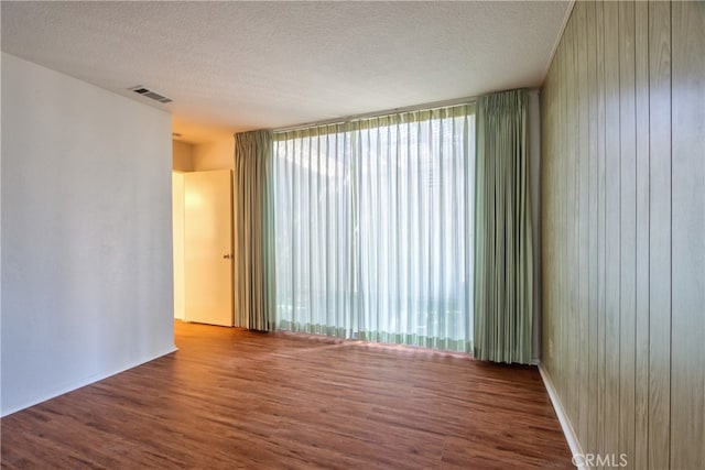 unfurnished room with floor to ceiling windows, hardwood / wood-style floors, wood walls, and a textured ceiling