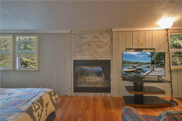 bedroom with hardwood / wood-style flooring, wooden walls, a textured ceiling, and a brick fireplace