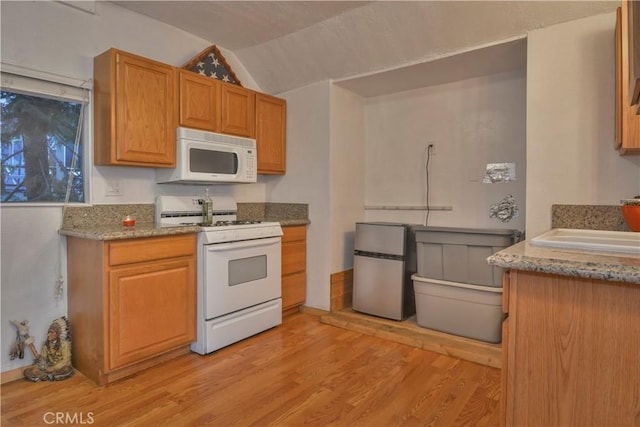 kitchen featuring sink, light stone counters, lofted ceiling, white appliances, and light wood-type flooring