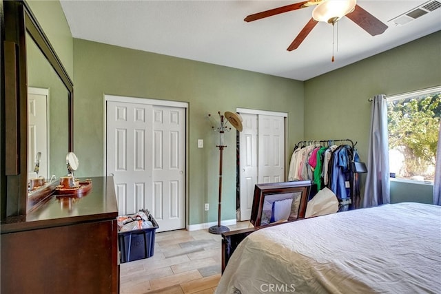 bedroom with ceiling fan, two closets, and light hardwood / wood-style flooring