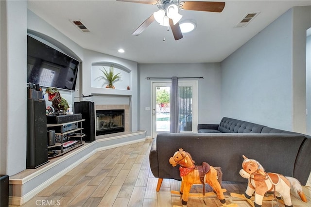 living room featuring ceiling fan, light hardwood / wood-style flooring, and a tile fireplace