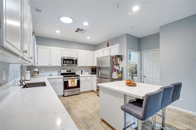 kitchen featuring stainless steel appliances, sink, light hardwood / wood-style floors, white cabinetry, and a kitchen bar