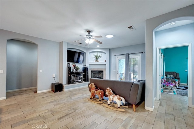 living room featuring light wood-type flooring, ceiling fan, and a tile fireplace