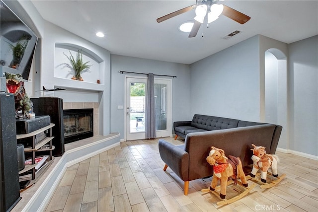 sitting room with light wood-type flooring, ceiling fan, and a tile fireplace