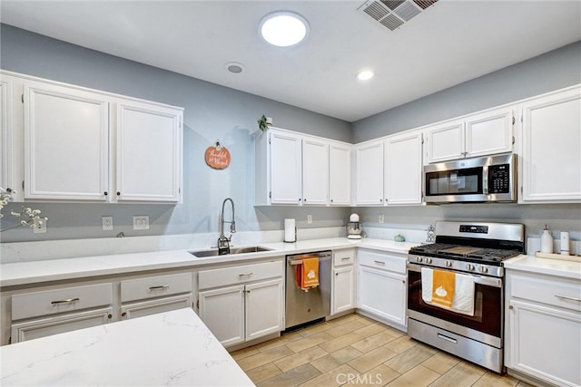 kitchen featuring appliances with stainless steel finishes, light stone counters, sink, and white cabinets