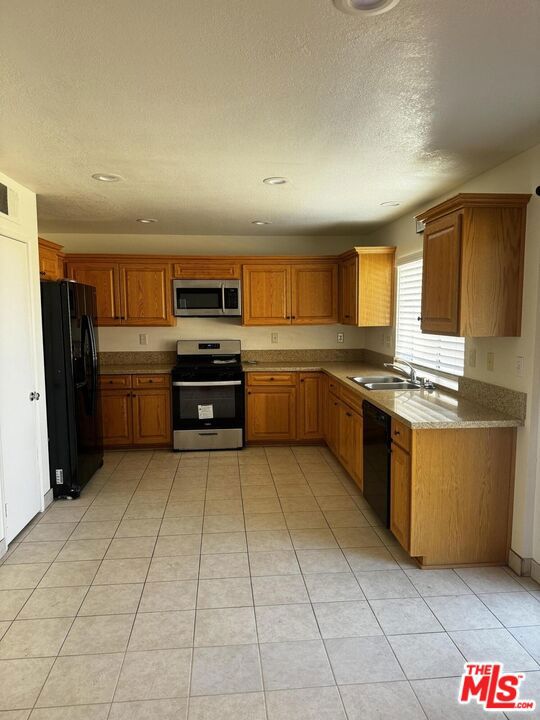 kitchen featuring light stone counters, light tile patterned floors, sink, a textured ceiling, and black appliances