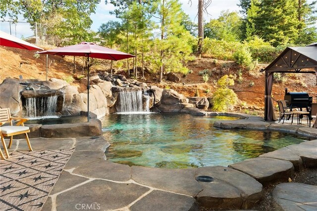 view of swimming pool with pool water feature and grilling area